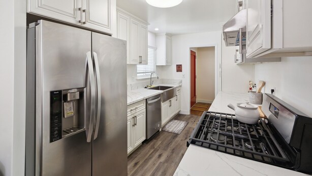 A modern kitchen with stainless steel appliances, white cabinetry, and a marble countertop. - Modern Relaxing Retreat With Private Pool 4 Bedroom Home by RedAwning (Azusa)