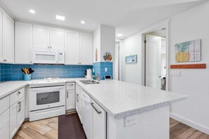 A modern kitchen with white cabinets, a blue backsplash, and a large island.