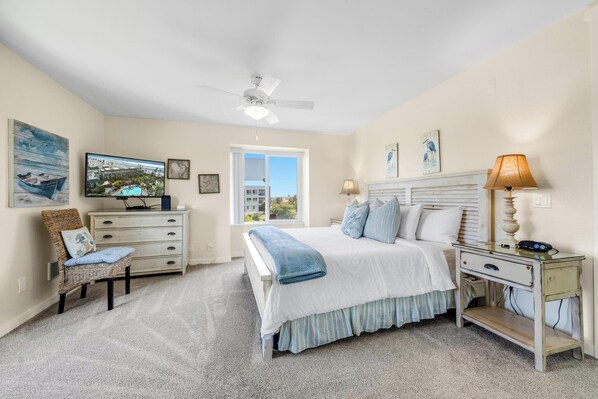 A bedroom with a bed, a desk, a chair, a TV, and a ceiling fan.