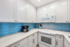 Eine Küche mit weißen Schränken, einer blauen Fliesenrückwand, einer Kaffeemaschine und einer Mikrowelle.
