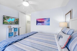 A bedroom with a bed, a ceiling fan, a wall-mounted TV, and a painting.