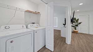 Une buanderie avec deux machines à laver blanches, un étendoir et une plante en pot.