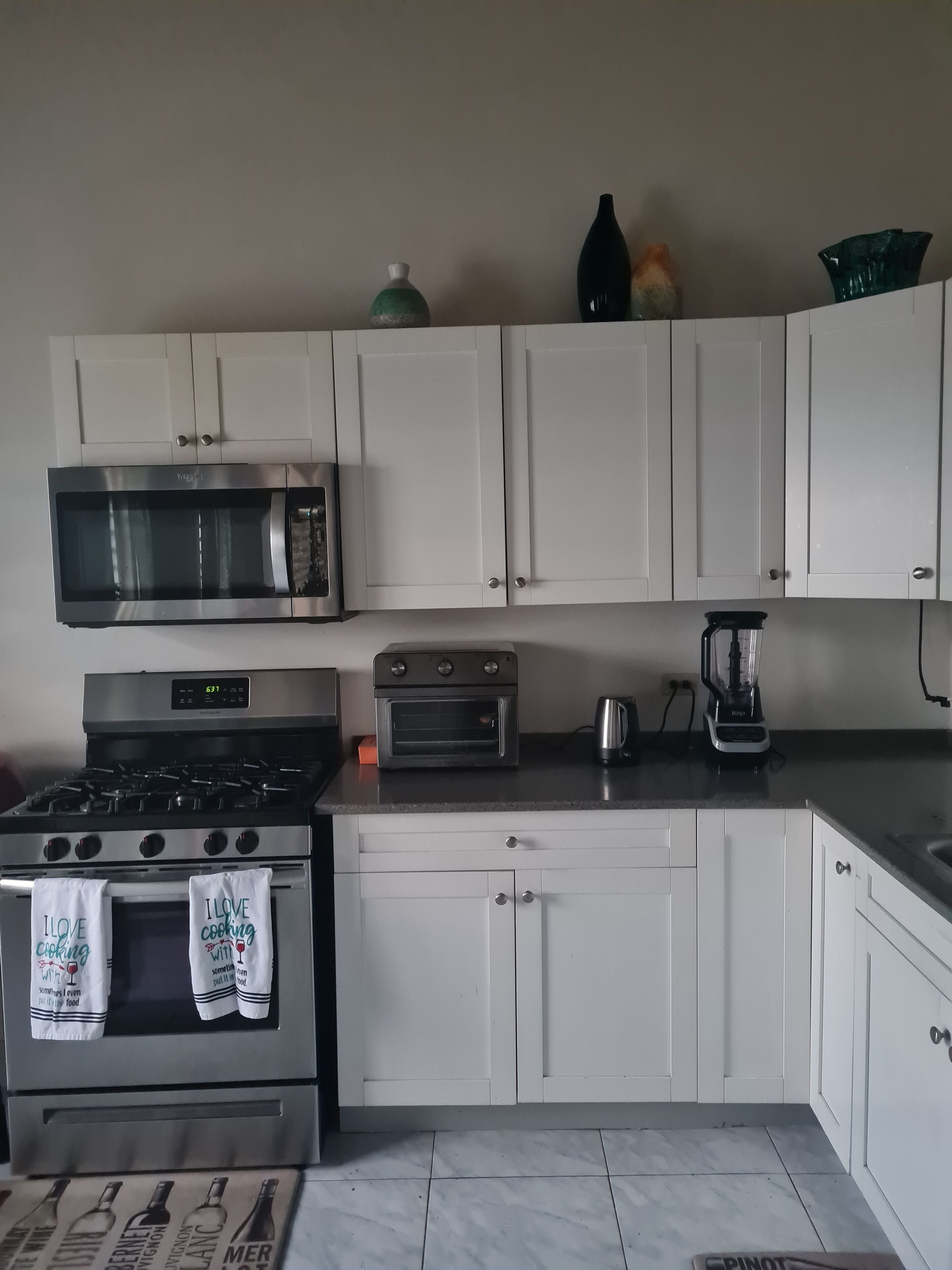 A kitchen with white cabinets, a stainless steel stove, a microwave, an oven, and a coffee maker.