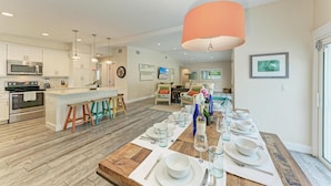 Una cocina moderna con armarios blancos, una isla central con taburetes y un comedor listo para una comida.