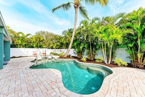 Una piscina a bordo curvo, circondata da un patio in mattoni e rigogliosa vegetazione tropicale.