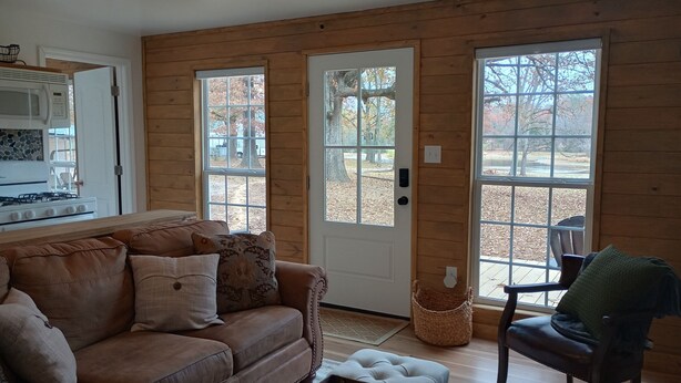 Un intérieur de chalet chaleureux, avec un revêtement mural en bois, un canapé, un fauteuil et un coin cuisine équipé d’une cuisinière et d’un four à micro-ondes.