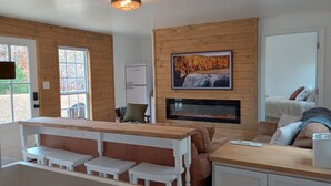 L’intérieur chaleureux d’un chalet avec un coin repas en bois, une cheminée et un lit à l’arrière-plan.