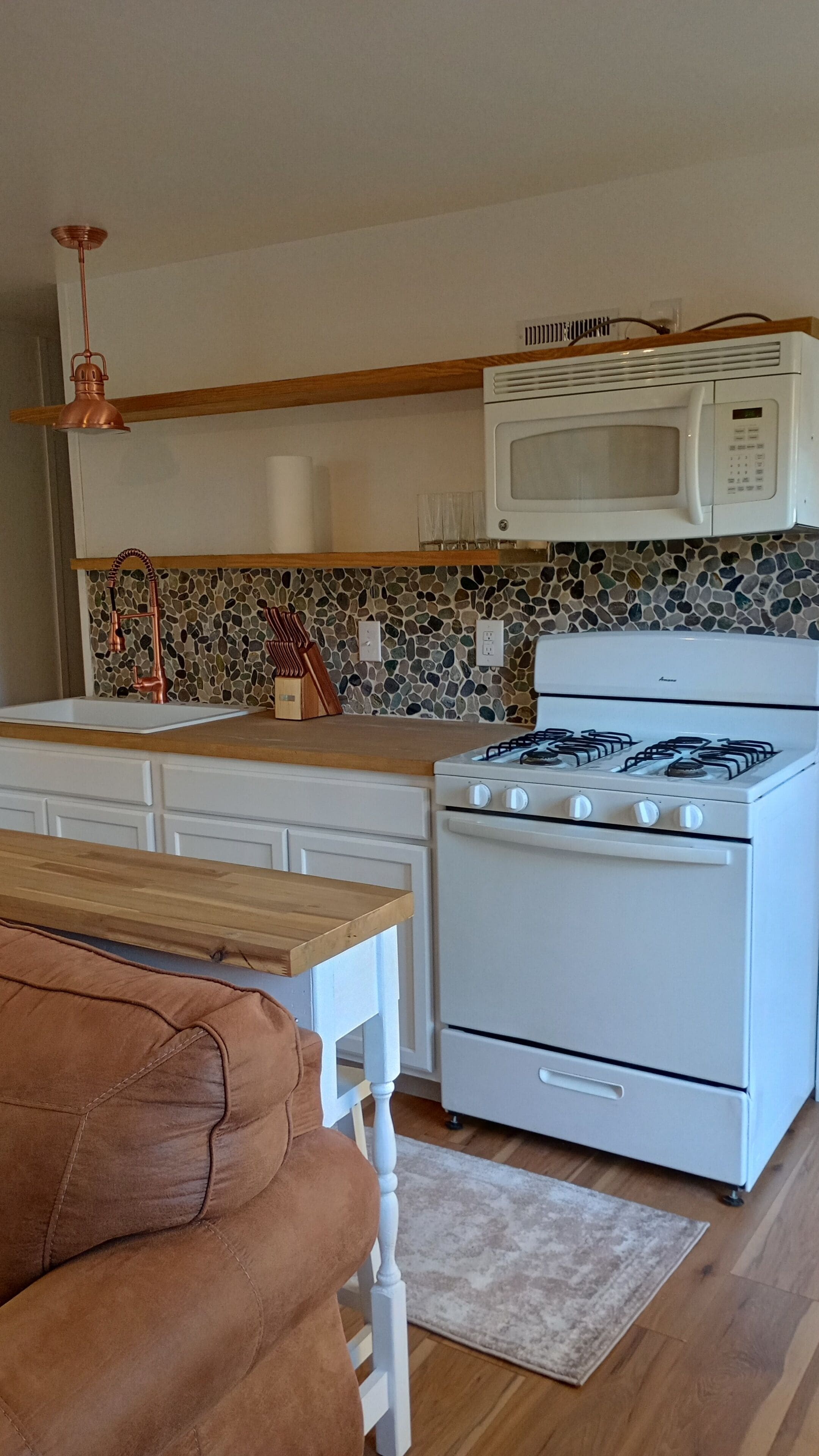 Cozinha com fogão branco, micro-ondas e pia. Apresenta bancada de madeira e painel de parede com padrão.