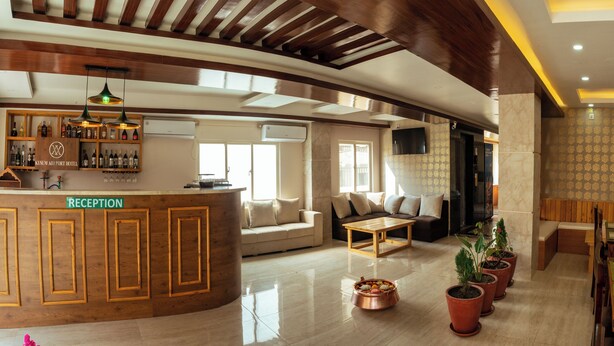 Ein Hotel-Empfangsbereich mit einem Holzbüro, einer Bar mit Spirituosenflaschen, einer Sitzecke mit Sofas und einem Couchtisch sowie einem Essbereich mit Tisch für zwei Personen.