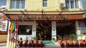 Das äußere Erscheinungsbild des Kusum Airport Hotels mit einladendem Eingang, mehreren Kübelpflanzen und einem Schild mit dem Hotelnamen.