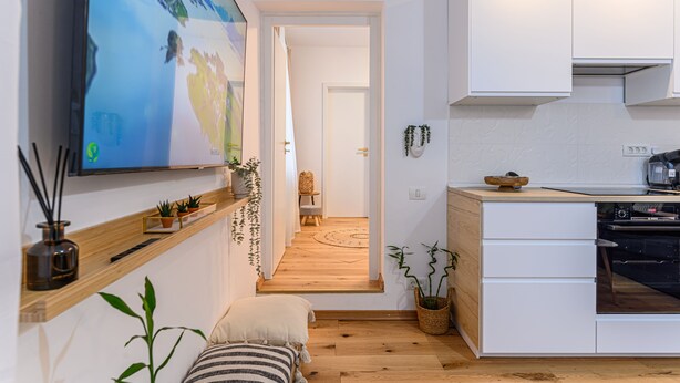 A modern kitchen with white cabinets, a built-in oven, and a wooden countertop. There is a TV mounted on the wall displaying a scenic image. - Peles Castle Boutique Home - Close to City Center (Sinaia)