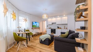 A modern living room with a sofa, chairs, a dining table, and a kitchen area. - Peles Castle Boutique Home - Close to City Center (Sinaia)