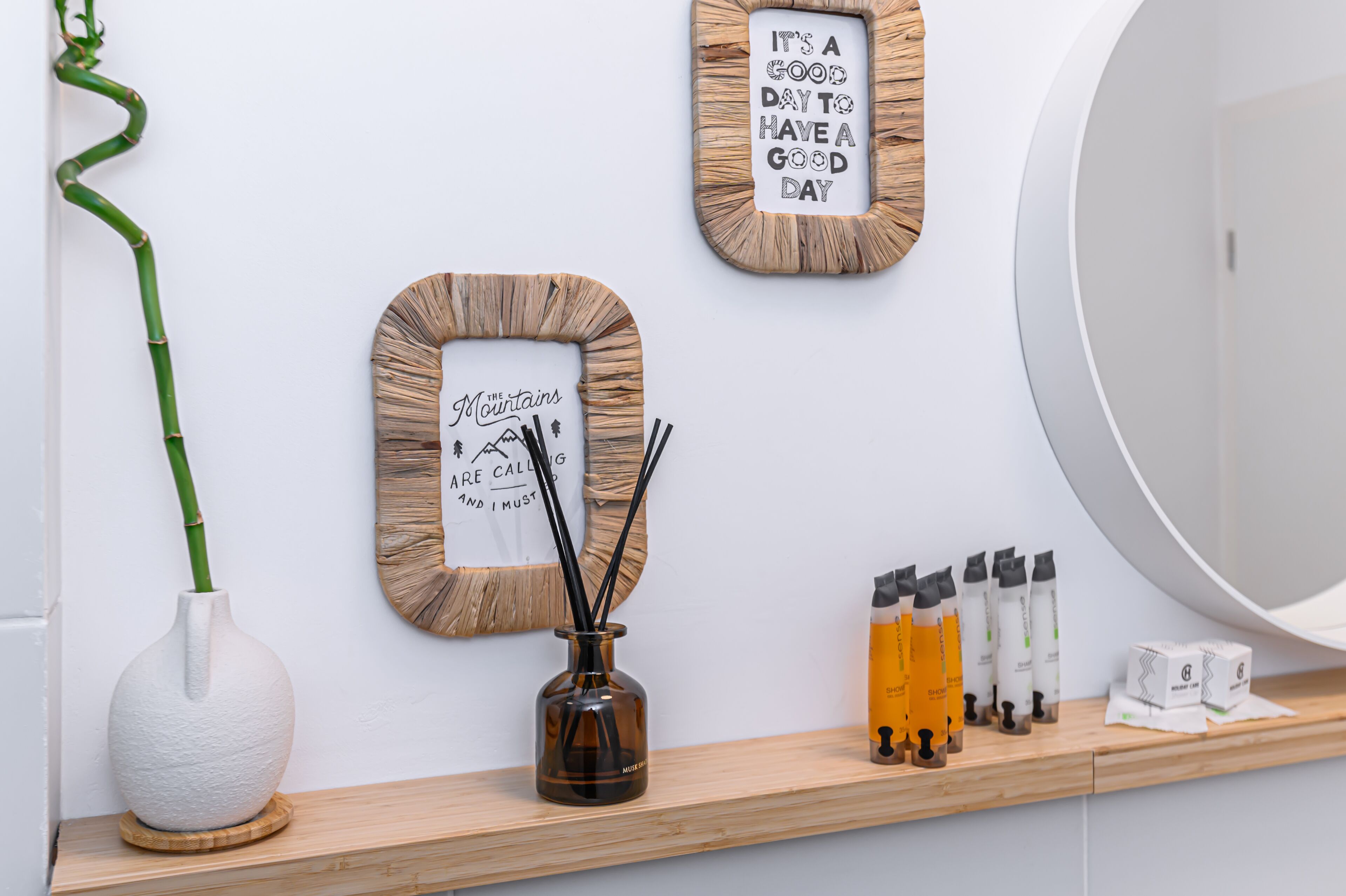 A bathroom with a mirror, a shelf with toiletries, and two framed pictures on the wall.