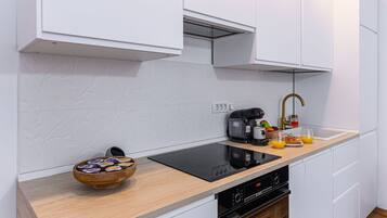 A modern kitchen with white cabinets, a wooden countertop, an induction cooktop, a coffee maker, a sink with a gold faucet, and a bowl of snacks.