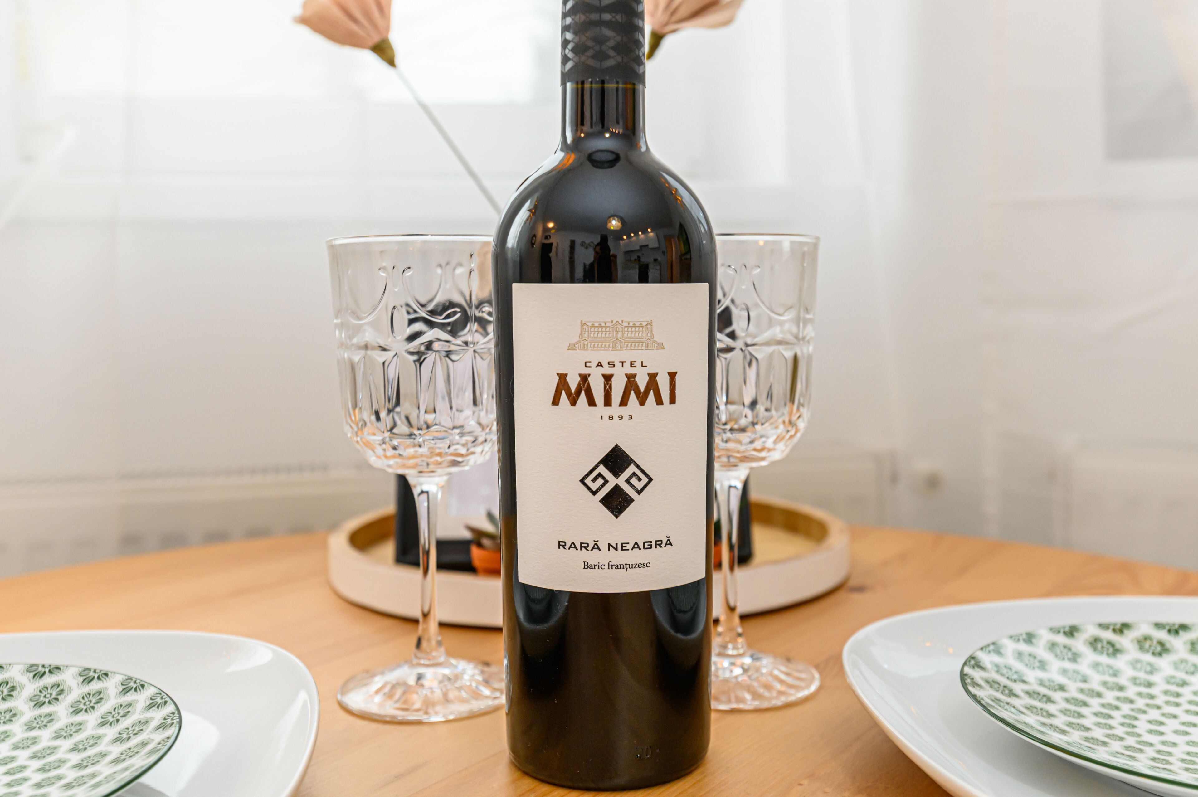 Una botella de vino Castel Mimi sobre una mesa con dos copas y platos.