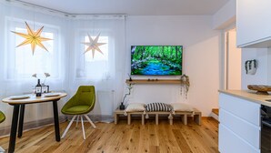 A modern living room with a wooden floor, a green chair, a bench, a TV on the wall, and a star-shaped hanging light. - Peles Castle Boutique Home - Close to City Center (Sinaia)