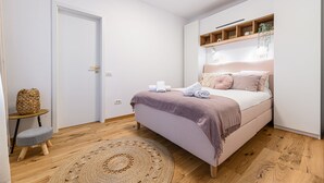 A bedroom with a bed, bedside tables, a small stool, a woven rug, and a door. - Peles Castle Boutique Home - Close to City Center (Sinaia)