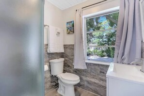 Une salle de bain comprenant des toilettes, des murs en marbre, une fenêtre avec des rideaux, un lavabo et un porte-serviettes.