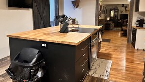 A modern kitchen with a wooden island, black trash bin, and a mounted deer skull on the wall. - Outdoorsman's Paradise Sleeps 9 in Cedar (Cedar)