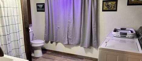 A bathroom with a toilet, a sink, a shower curtain, and a laundry machine.
