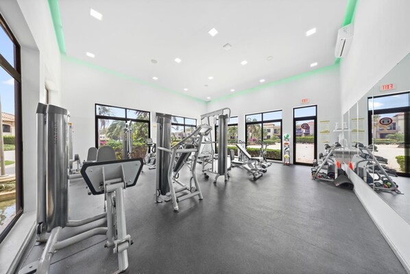 Un gimnasio moderno con varias máquinas de ejercicio, ventanas amplias y una señal de salida.