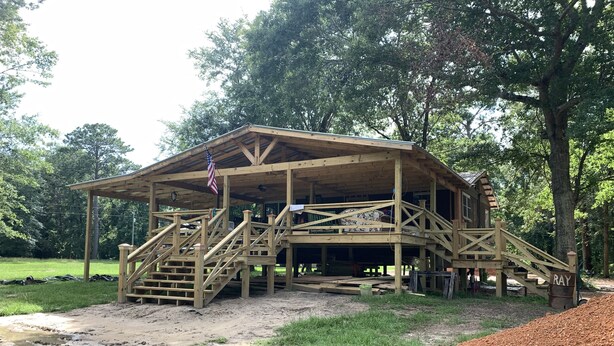 A wooden pavilion with a covered porch, a flag, and a ramp leading to a deck.