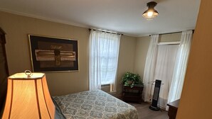 A bedroom with a bed, a nightstand, a lamp, a framed picture on the wall, and a window with curtains.