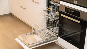 Uma cozinha com lava-louças e forno, armários brancos e chão de azulejos.