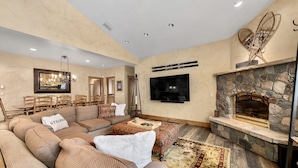 A spacious living room with a stone fireplace, a large flat-screen TV, and a cozy seating area with patterned sofas and a rug. - Steamboat in Style! Dog Friendly, Walk to Resort, Hot Tub, Great Views, Locker (Steamboat Springs)