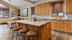 A spacious kitchen with wooden cabinets, a large island with stools, and a view of the outdoors. - Steamboat in Style! Dog Friendly, Walk to Resort, Hot Tub, Great Views, Locker (Steamboat Springs)