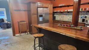 Una cocina con armarios de madera, un refrigerador de acero inoxidable, una encimera de madera y dos taburetes.