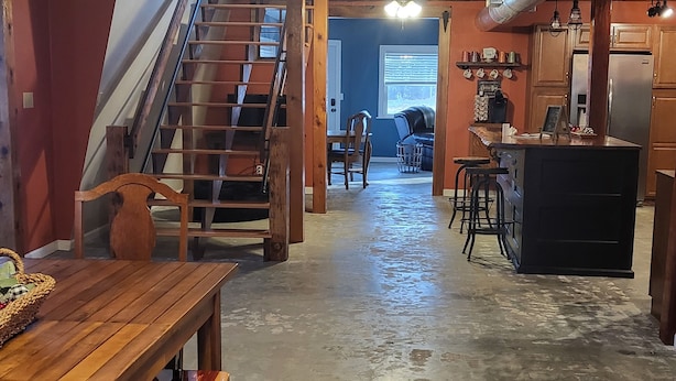 Una cocina amplia con una isla central, un comedor con mesa y banco de madera, y una escalera que conduce a un nivel superior.
