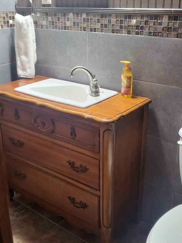 A bathroom with a wooden vanity, a white sink, and a bottle of soap.