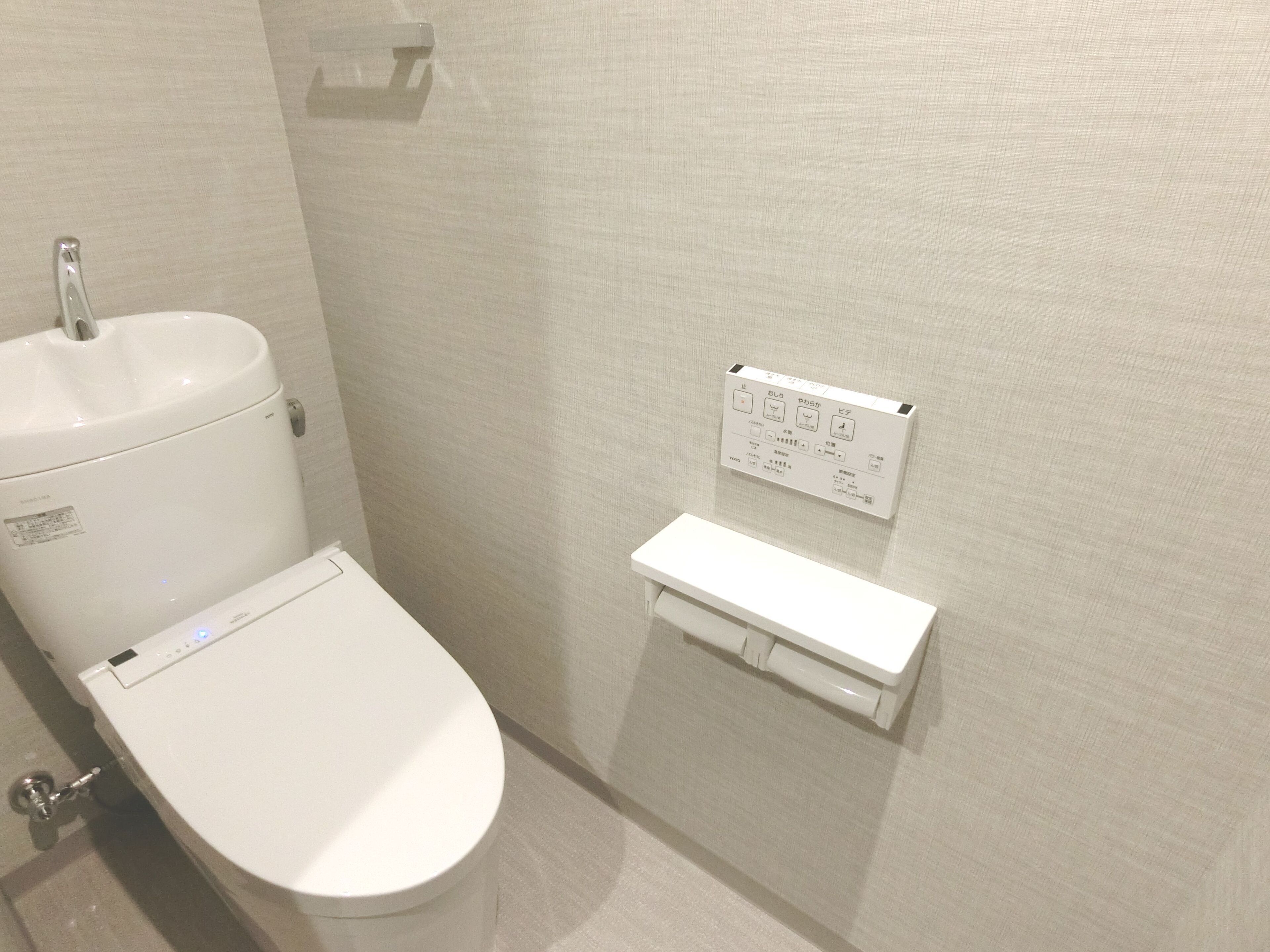 A modern bathroom with a toilet, a wall-mounted control panel, and a small shelf.