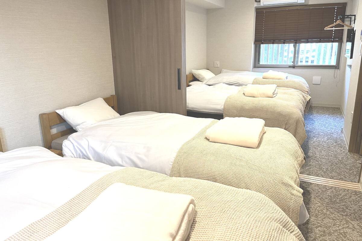 A hotel room with three beds, a wardrobe, a mirror, and a window with blinds.