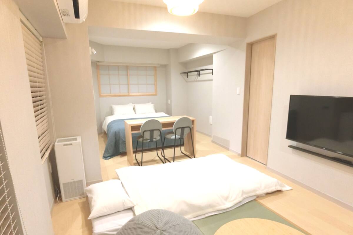 A compact hotel room with a bed, a desk with chairs, a television, and a small seating area.