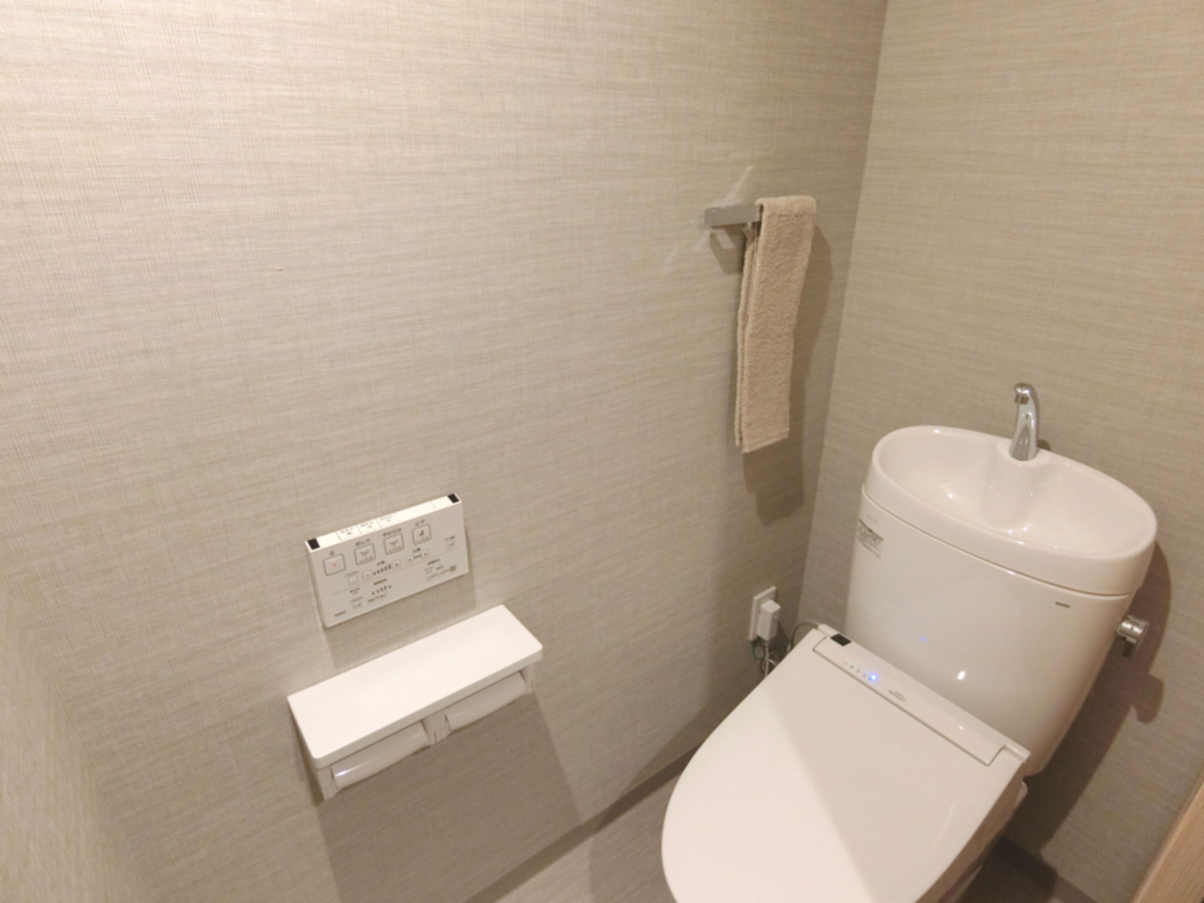 A bathroom with a toilet, a towel hanging on a rack, and a control panel on the wall.