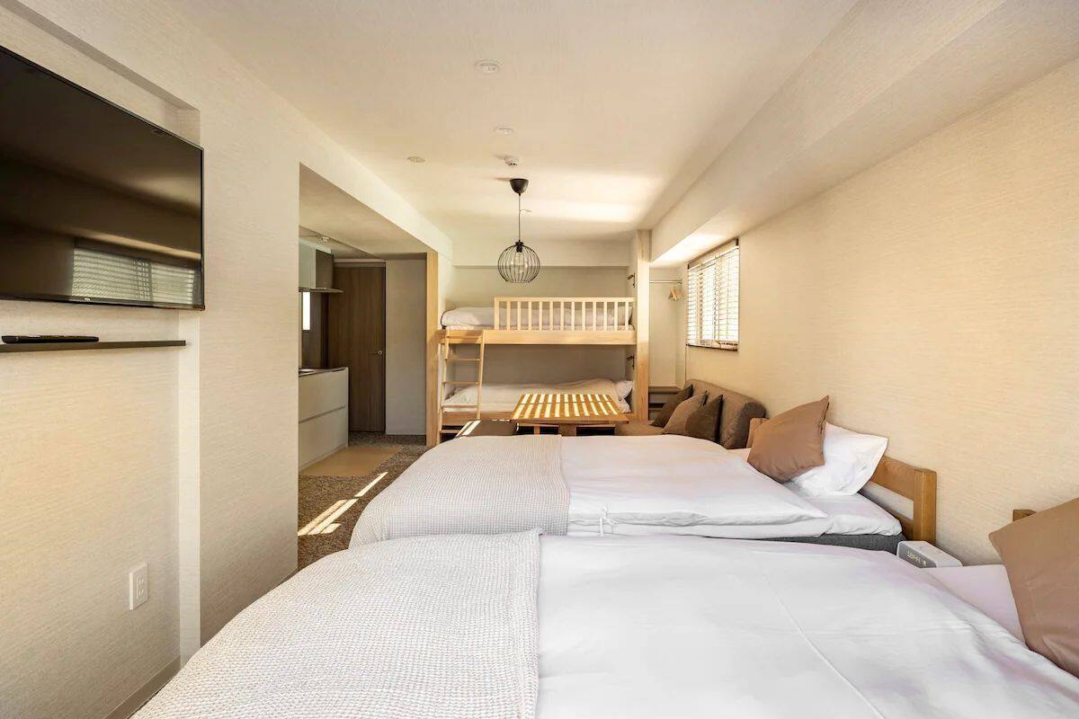 A hotel room with two beds, a TV, a bunk bed, and a dining area.