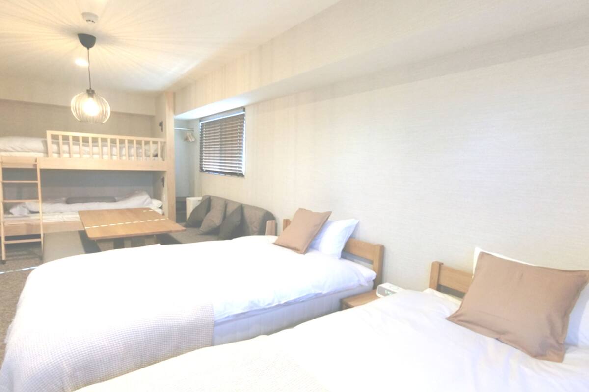 A room with two single beds, a bunk bed, a wooden table, and a hanging light fixture.