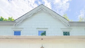 Une maison à deux étages avec une porte d’entrée en bois foncé, deux fenêtres à l’étage supérieur et un petit porche agrémenté de plantes en pot.