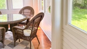 Une pièce dotée d'une grande fenêtre, de chaises en osier, d'une table ronde et d'un ventilateur de plafond.