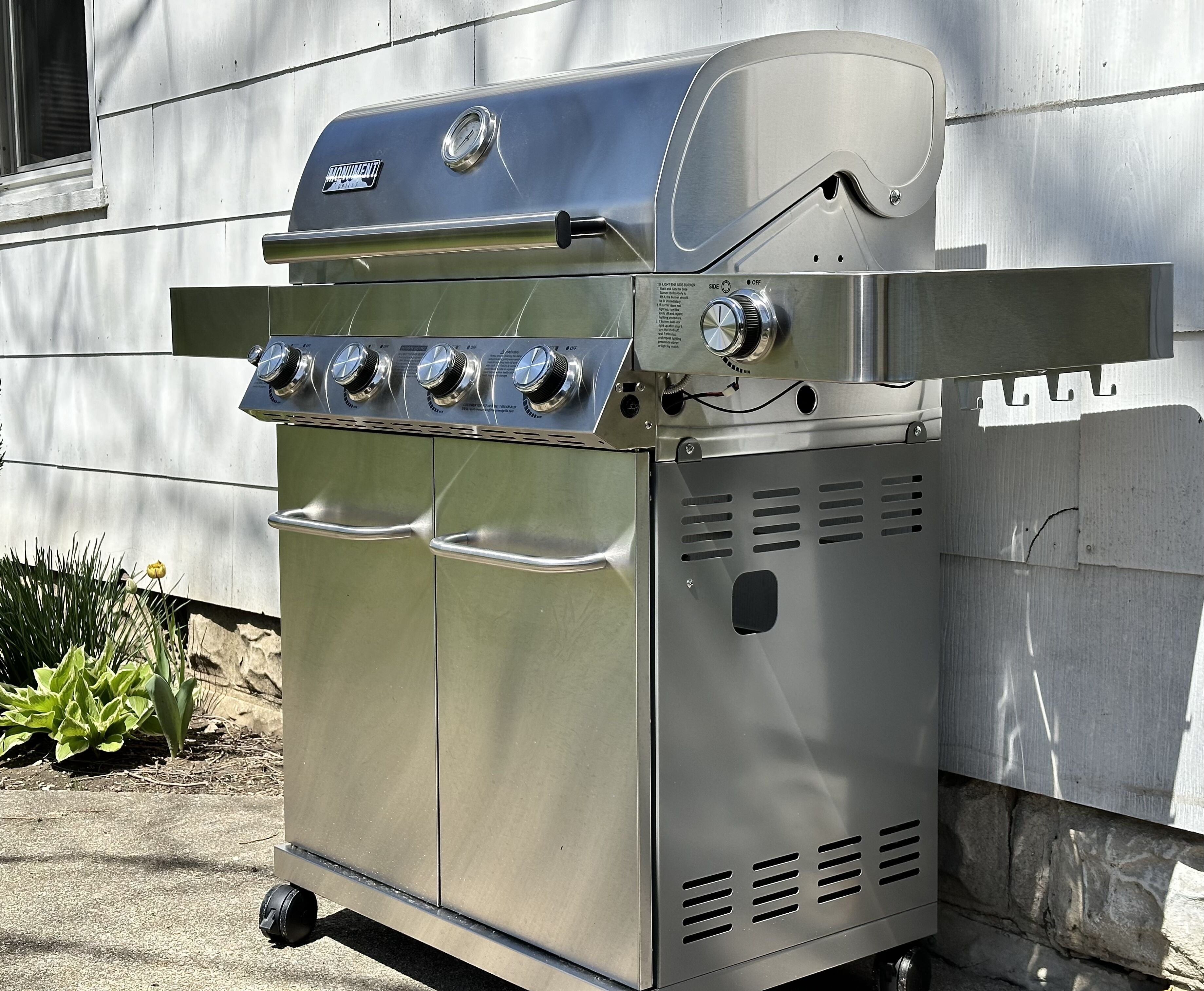 A stainless steel outdoor grill with four burners, a control panel, and a side shelf.