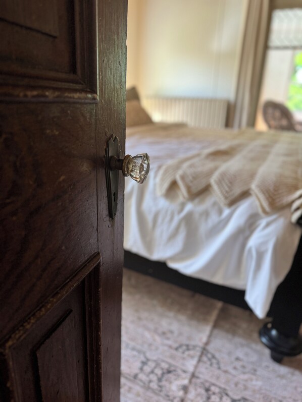 Una puerta de madera con pomo de cristal, que da a un dormitorio con cama, una silla y suelo estampado.