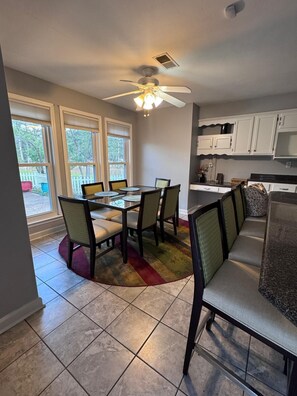 A dining area with a round table and six chairs, a ceiling fan, and a kitchen area with white cabinets.