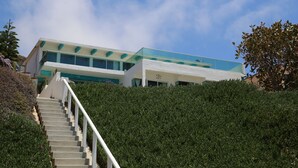 A modern building with a glass facade, a staircase leading up to it, and a well-maintained hedge in the foreground.