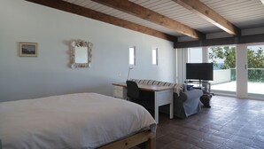 A bedroom with a bed, a desk, a chair, a television, and a balcony with a view.