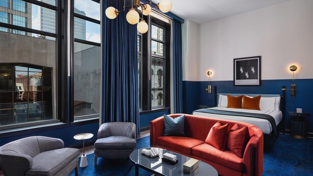 A hotel room with a large bed, a red sofa, a grey armchair, a glass coffee table, and a modern chandelier. - 1-Bedroom Suite at a 4⭐️ Hotel (Nashville)