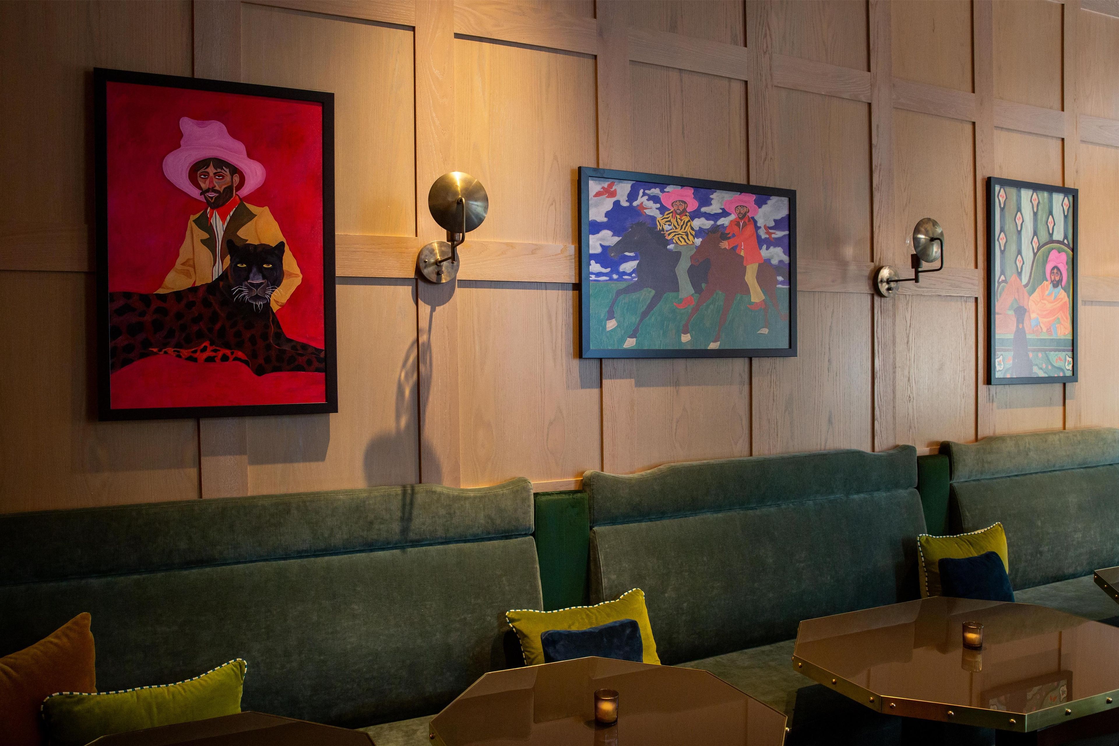 L’intérieur d’un restaurant avec des murs lambrés en bois, des sièges rembourrés de couleur verte et des œuvres d’art encadrées accrochées aux murs.