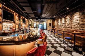 Un bar con suelo a cuadros, taburetes y una barra larga con botellas y vasos.
