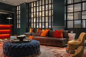 Una sala de estar moderna con un sofá, un reposapiés y sillones, un tapete estampado y un ventanal con persianas.